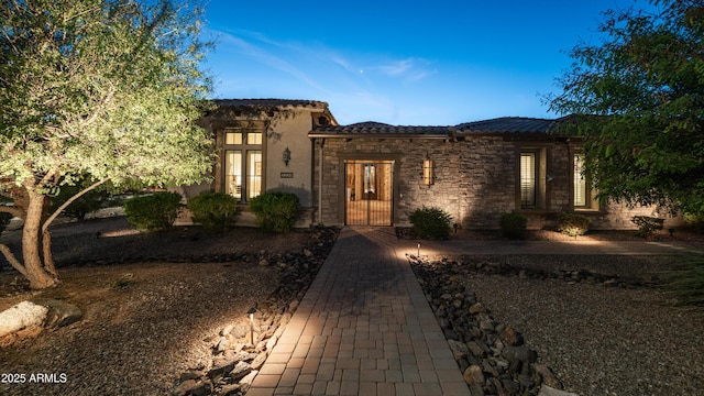 view of front of property with stone siding, french doors, a tiled roof, and stucco siding