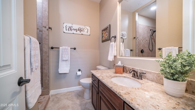 bathroom featuring baseboards, tiled shower, vanity, and toilet