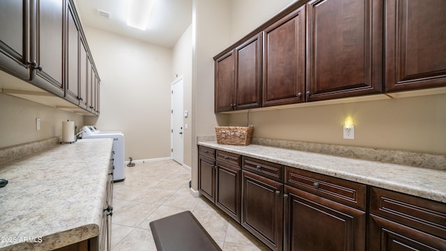 interior space with light tile patterned floors, visible vents, baseboards, washer and dryer, and cabinet space