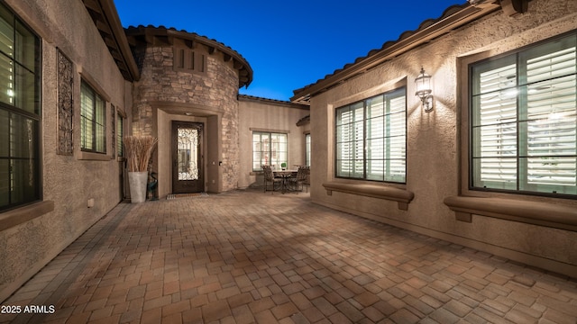 view of exterior entry with stucco siding, a tiled roof, and a patio