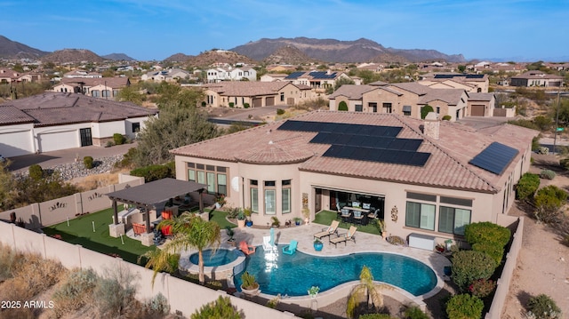 rear view of house featuring a patio, a fenced backyard, a residential view, roof mounted solar panels, and a mountain view