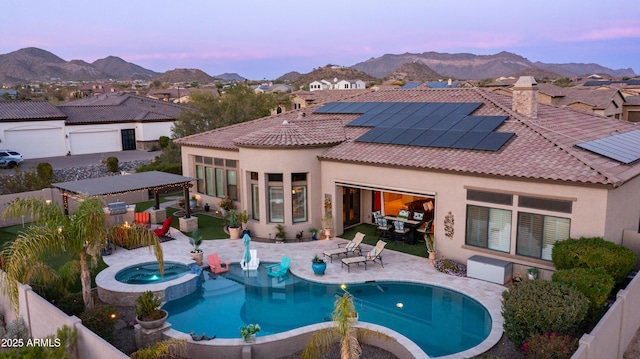 back of property at dusk featuring solar panels, a patio area, a mountain view, and stucco siding