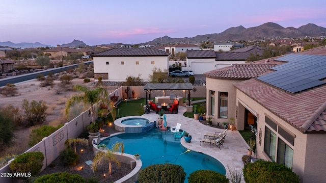 pool at dusk with a pool with connected hot tub, a patio area, a fenced backyard, and a mountain view