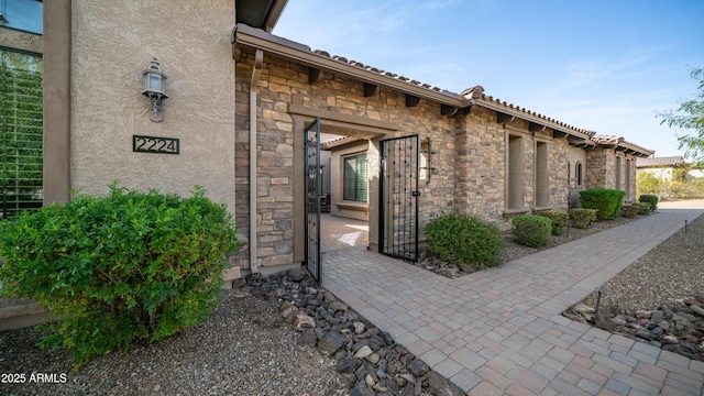 doorway to property with stone siding, a tiled roof, and stucco siding