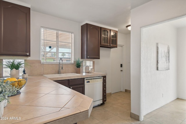 kitchen featuring dishwasher, dark brown cabinets, sink, and light tile patterned floors