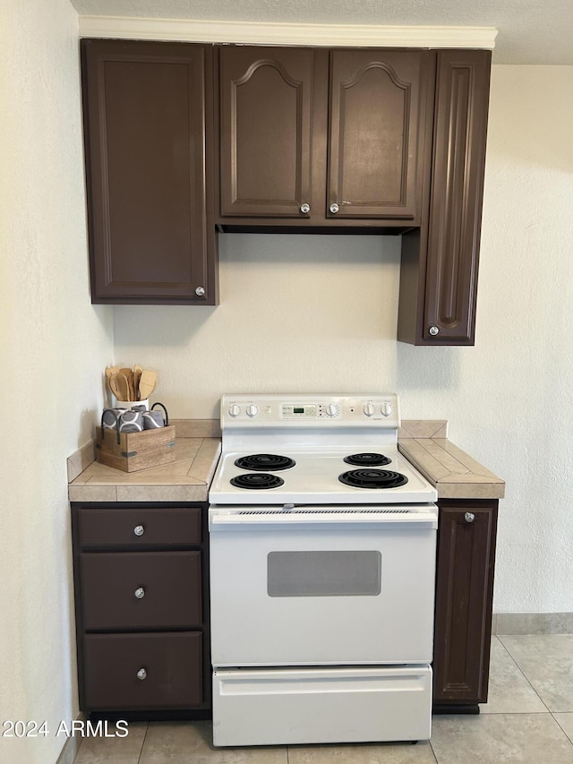 kitchen with white electric range oven, dark brown cabinets, and light tile patterned flooring