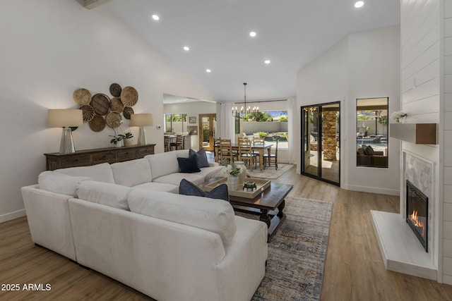 living area featuring high vaulted ceiling, a high end fireplace, a chandelier, light wood-type flooring, and baseboards