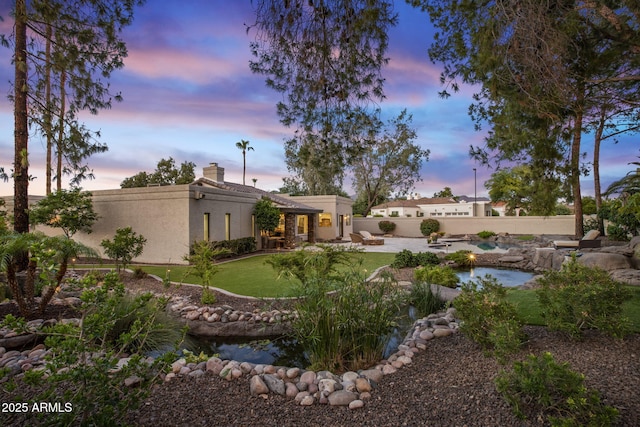 yard at dusk featuring a garden pond, a fenced backyard, and a patio