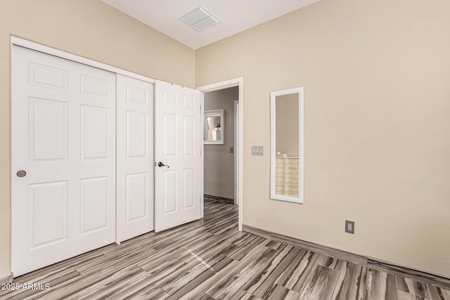 unfurnished bedroom with a closet, visible vents, baseboards, and wood finished floors