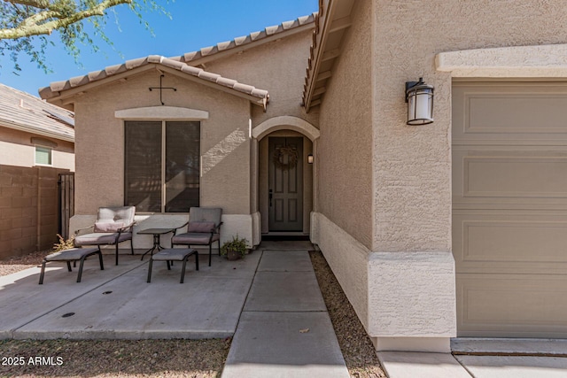 entrance to property featuring a tiled roof, stucco siding, a garage, and fence