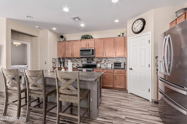 kitchen featuring visible vents, dark stone countertops, backsplash, appliances with stainless steel finishes, and a breakfast bar area