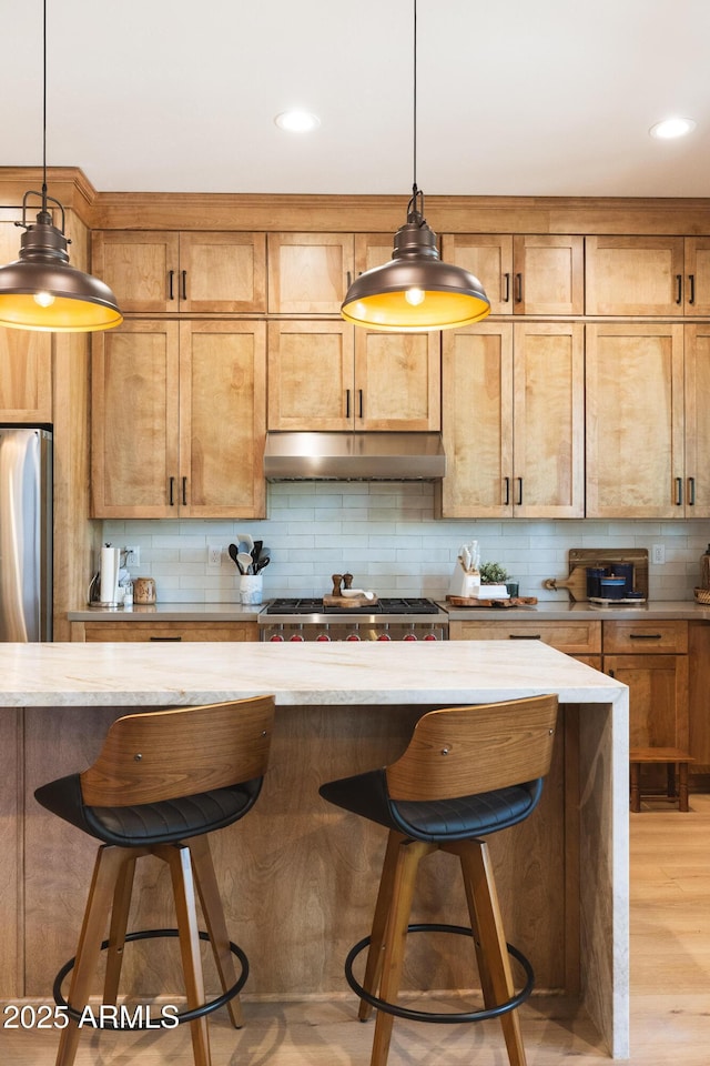 2582 S Cottonrose Ln, Flagstaff, AZ 86001 - kitchen with freestanding refrigerator, under cabinet range hood, tasteful backsplash, a breakfast bar, and decorative light fixtures