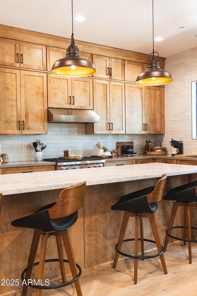 2582 S Cottonrose Ln, Flagstaff, AZ 86001 - kitchen with under cabinet range hood, tasteful backsplash, a breakfast bar, and decorative light fixtures