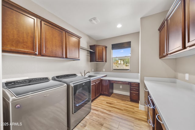 laundry area with washer and clothes dryer, sink, light hardwood / wood-style flooring, and cabinets