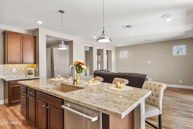 kitchen featuring dishwasher, decorative backsplash, sink, light wood-type flooring, and a kitchen island with sink