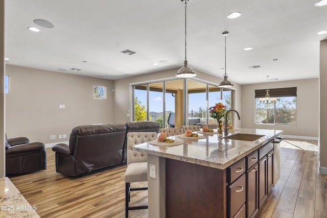 kitchen featuring light stone countertops, sink, hanging light fixtures, light hardwood / wood-style flooring, and dark brown cabinets