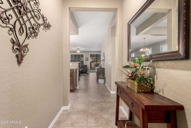 hall featuring a textured wall, baseboards, an inviting chandelier, and light tile patterned floors