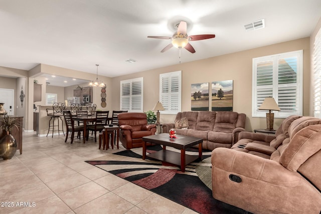 living area with light tile patterned floors, baseboards, visible vents, and ceiling fan with notable chandelier