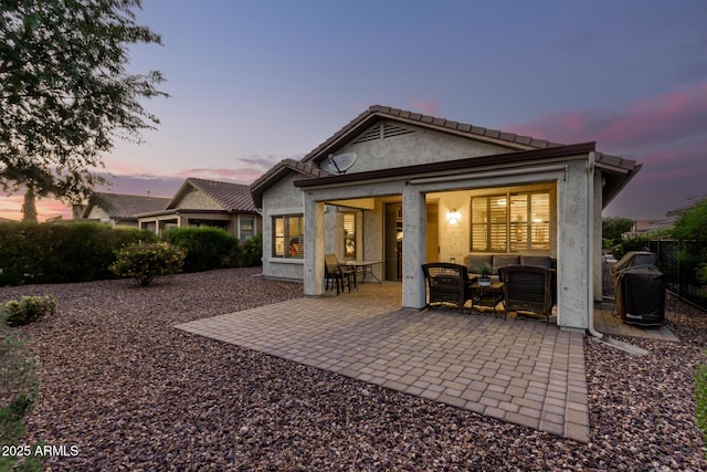 back of property at dusk with a patio, outdoor lounge area, and stucco siding