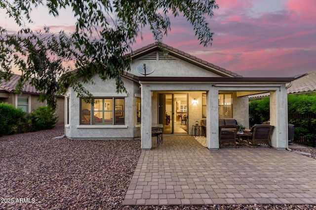 back of house at dusk featuring a patio area and stucco siding