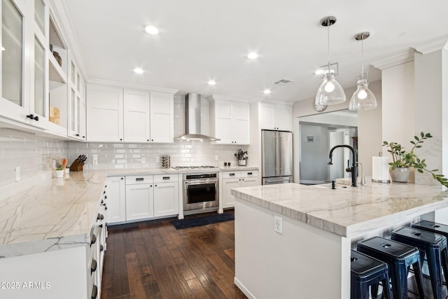 kitchen with white cabinetry, appliances with stainless steel finishes, wall chimney range hood, light stone counters, and sink