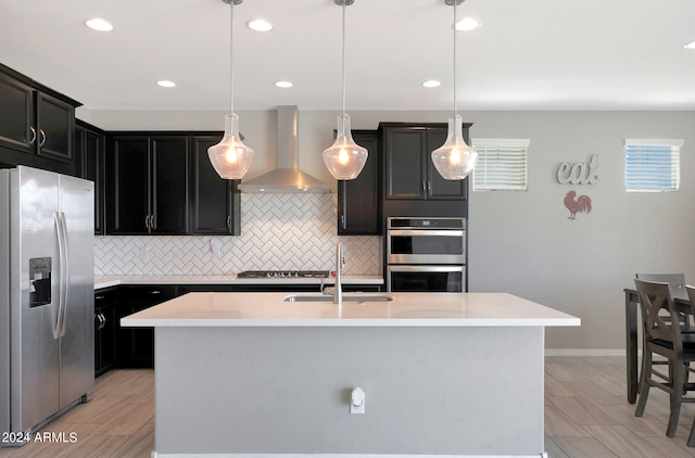 kitchen featuring a center island with sink, stainless steel appliances, and wall chimney range hood