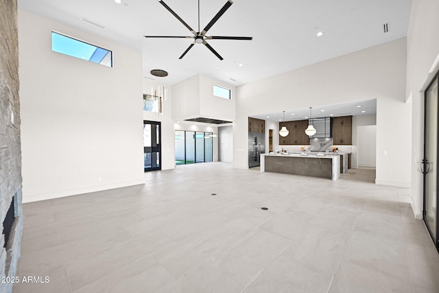 unfurnished living room with visible vents, a ceiling fan, a high ceiling, a fireplace, and baseboards