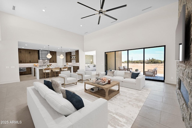 living area featuring visible vents, a towering ceiling, recessed lighting, a stone fireplace, and ceiling fan