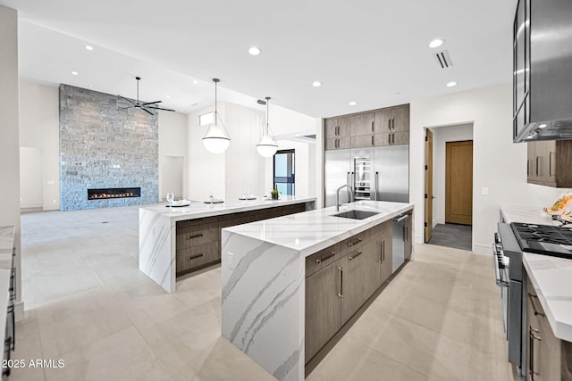 kitchen featuring a sink, a stone fireplace, a large island, high quality appliances, and modern cabinets