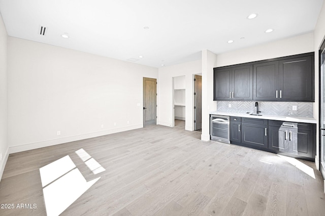 interior space with backsplash, baseboards, beverage cooler, indoor wet bar, and light wood-style floors