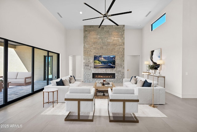 living room featuring visible vents, a ceiling fan, a high ceiling, a stone fireplace, and baseboards