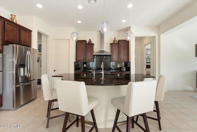 kitchen featuring wall chimney range hood, stainless steel fridge with ice dispenser, backsplash, decorative light fixtures, and a center island with sink