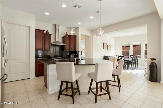 kitchen with pendant lighting, backsplash, a center island with sink, wall chimney range hood, and light tile patterned floors