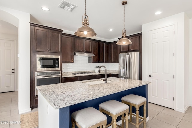 3910 E Turley St, Gilbert, AZ 85295 - kitchen featuring stainless steel appliances, a sink, light tile patterned flooring, dark brown cabinetry, and a breakfast bar