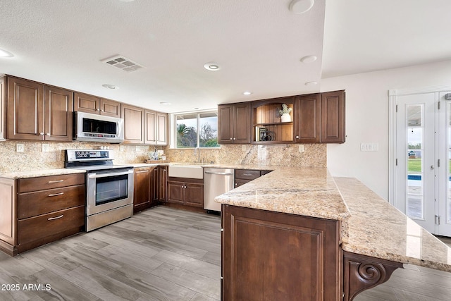 kitchen featuring open shelves, stainless steel appliances, visible vents, decorative backsplash, and a peninsula