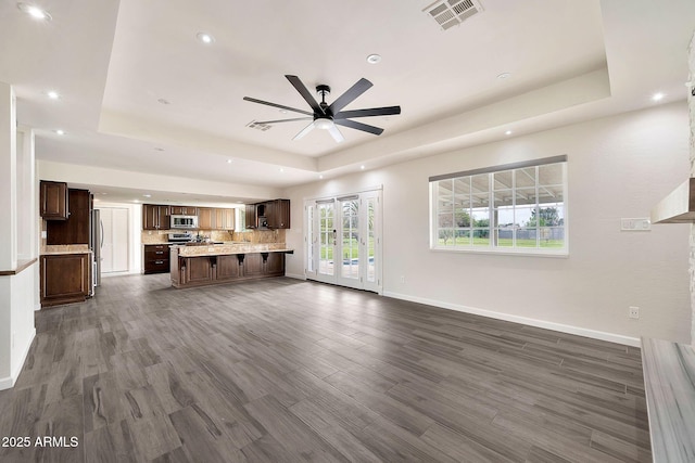 unfurnished living room with baseboards, visible vents, a ceiling fan, a raised ceiling, and dark wood finished floors