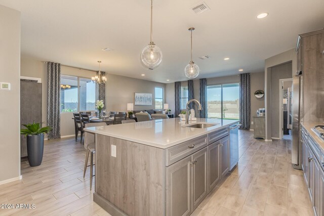 kitchen with light countertops, visible vents, appliances with stainless steel finishes, a sink, and an island with sink