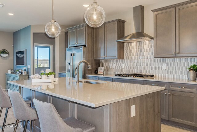 kitchen featuring stainless steel appliances, a sink, wall chimney range hood, decorative backsplash, and an island with sink