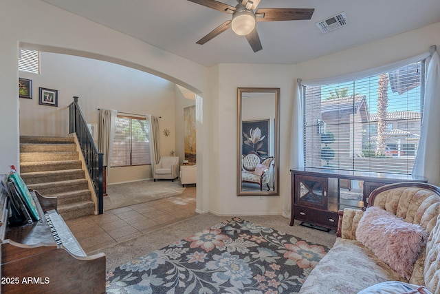 tiled living area featuring stairs, ceiling fan, plenty of natural light, arched walkways, and carpet