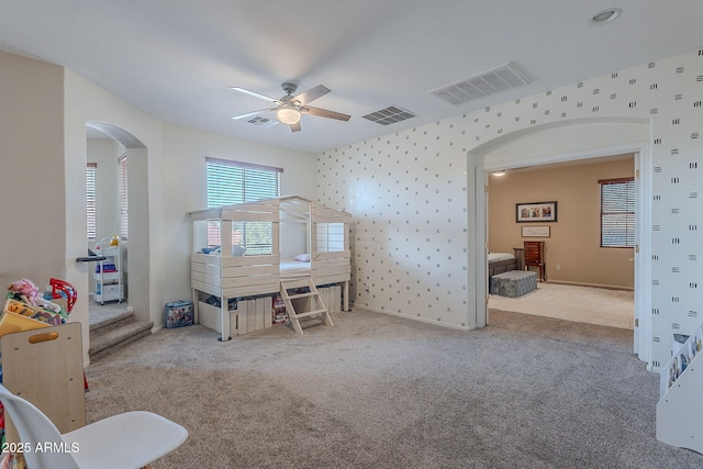 carpeted bedroom with visible vents, arched walkways, and wallpapered walls