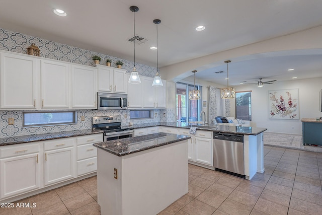 kitchen with a sink, light tile patterned floors, open floor plan, stainless steel appliances, and white cabinetry