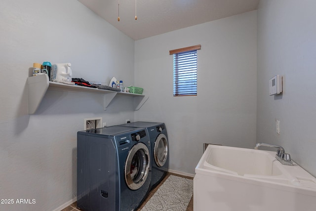 washroom featuring washing machine and clothes dryer, laundry area, a sink, and baseboards