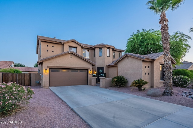 mediterranean / spanish house with fence, a tile roof, a garage, stucco siding, and driveway