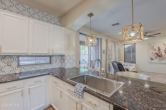 kitchen with decorative backsplash, visible vents, a sink, an inviting chandelier, and white cabinetry