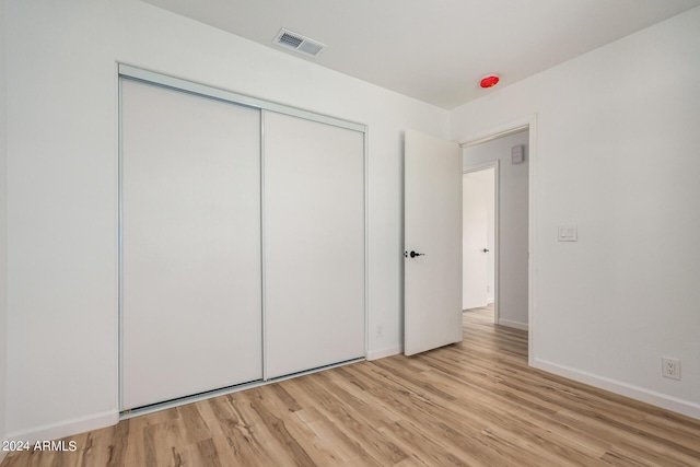 unfurnished bedroom featuring a closet, visible vents, light wood-style flooring, and baseboards