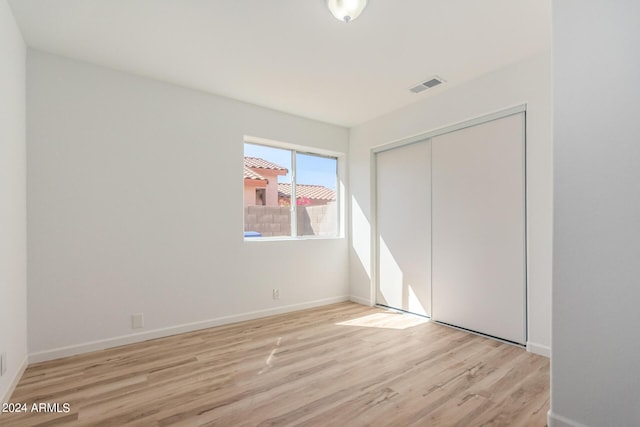 unfurnished bedroom with light wood-type flooring, visible vents, baseboards, and a closet