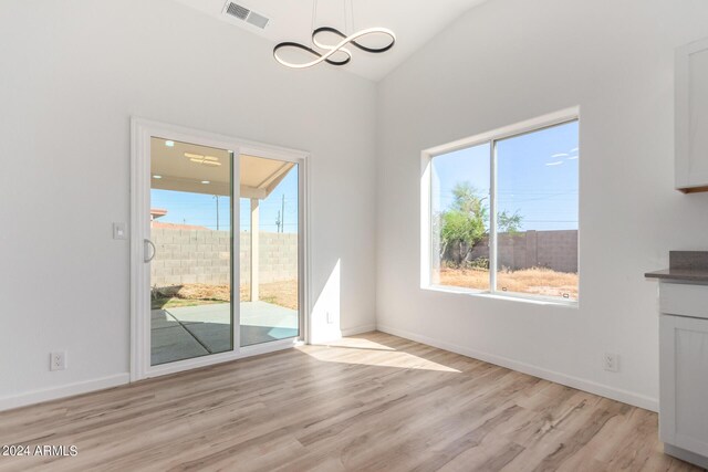 unfurnished dining area featuring vaulted ceiling, a chandelier, and light hardwood / wood-style floors