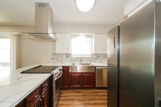 kitchen with island range hood, appliances with stainless steel finishes, light stone counters, a sink, and backsplash