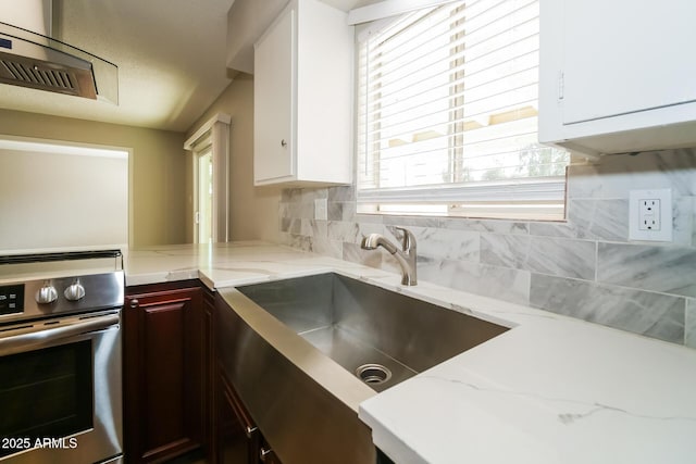 kitchen featuring white cabinets, stainless steel electric stove, light stone counters, and a sink