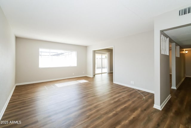 spare room with dark wood-type flooring, visible vents, and baseboards